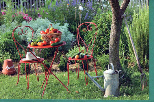 Blankokarte Gartenidylle mit rotem Bistrotisch, Stühlen, frischem Gemüse und Gießkanne für persönliche Grüße oder Einladungen