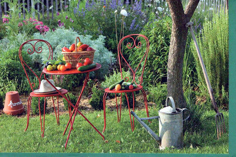 Blankokarte Gartenidylle mit rotem Bistrotisch, Stühlen, frischem Gemüse und Gießkanne für persönliche Grüße oder Einladungen