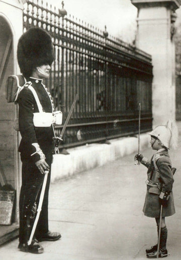 Humorvolle Postkarte im Retrostil - Soldat und Kind in Uniform mit Bärenfellmütze am Zaun, Schwarz - Weiß Fotografie