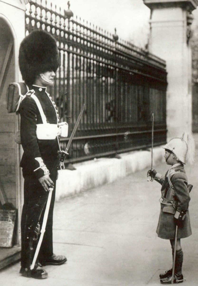 Humorvolle Postkarte im Retrostil - Soldat und Kind in Uniform mit Bärenfellmütze am Zaun, Schwarz - Weiß Fotografie