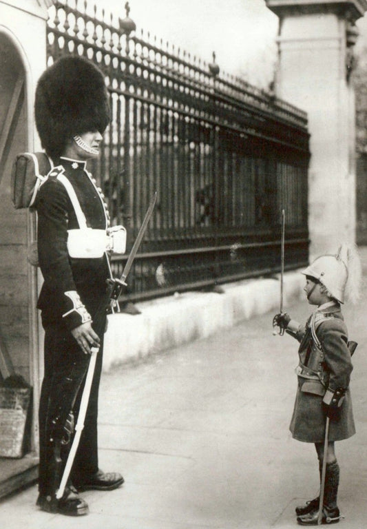 Humorvolle Postkarte im Retrostil - Soldat und Kind in Uniform mit Bärenfellmütze am Zaun, Schwarz - Weiß Fotografie