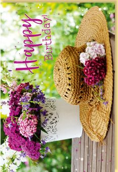 Geburtstagskarte mit sommerlichem Blumenarrangement und Strohhut auf Holztisch